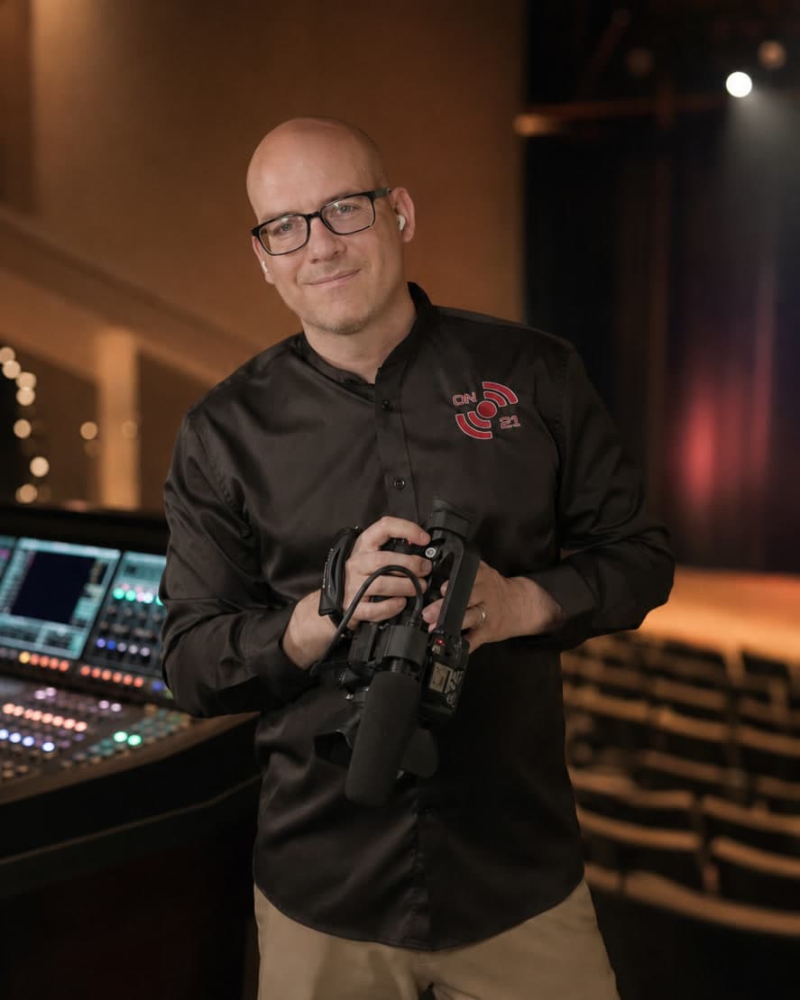 Zachary McKenzie, Founder and Lead Producer of ON21 Productions, holding a video camera in a performing arts venue
